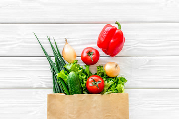 Healthy food with fresh vegetables in paper bag on white wooden background top view