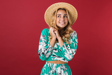 Excited young beautiful blonde cute woman in dress posing isolated over red wall background looking aside.