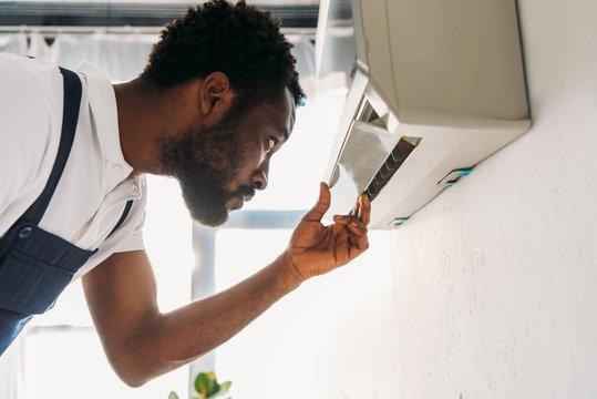 Concentrated African American Repairman Looking At Broken Air Conditioner