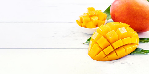 Beautiful chopped mango with green leaves on bright white color timber background. Above Top view, flat lay, copy space, close up. Tropical fruit concept.