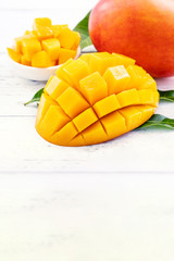 Beautiful chopped mango with green leaves on bright white color timber background. Above Top view, flat lay, copy space, close up. Tropical fruit concept.