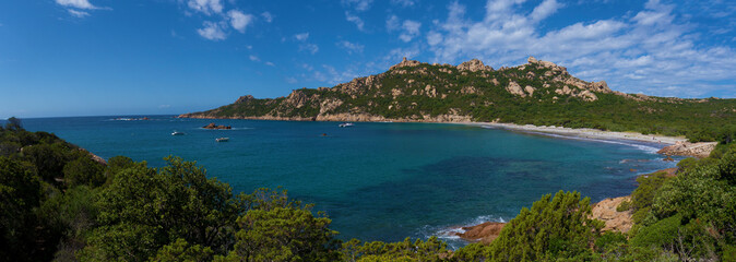 Fototapeta na wymiar A wide panorama shot of a sandy beach and a blue ocean bay surrounded by green hills in bright sunlight.