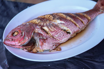 Fried sea fish on a white plate. Seafood in an outdoor cafe in Asia. Stock photo