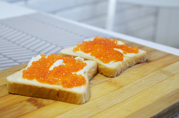 Sandwich with red caviar on a wooden cutting board.