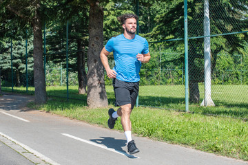 Handsome man running in park with trees in background