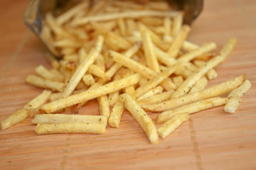 Snack french fries in foil pack. Fried potatoes are poured out of package on a wooden mat