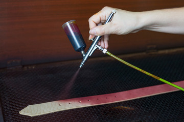 Leather craftsman causes paint on straps. Spray gun with purple paint. Handmade concept. Concept of...