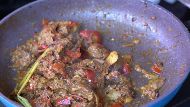 Frying pan with onion, lemongrass, red pepper and beef meat, close up. Indonesia. Sambal Goreng Ati Kentang, Indonesian cuisine, spicy beef meet and potatoes garnish with lemongrass leaf and red chili