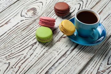 Full ceramic cup of hot black coffee near scattered sweet macaroons on old weathered rustic white table. Copy space
