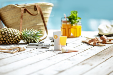 View on the wooden poolside with accessories for summer vacations, sunscreen lotions, drinks,...