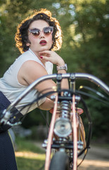 Fototapeta na wymiar A pinup woman in a vintage dress posed next to the old motorcycle