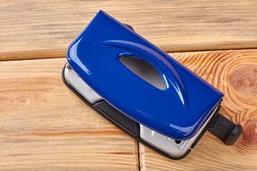 Office paper hole puncher. Blue paper hole puncher on wooden background. Metal stationery accessory.