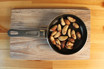 Brazil nuts are scattered on a small pan that stands on a wooden Board texture striped, close-up.