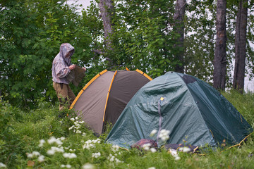 man covers the tent awning from the rain on the lake