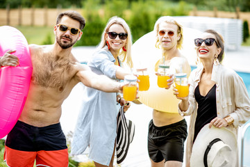 Group of happy friends having a party, dancing and drinking juice near the swimming pool during the summer time