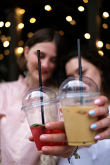 Two summer cocktails in plastic glasses are held by two friends. Ice coffee and berry lemonade.