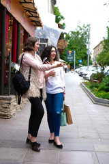 Two young girls walking, laughing and chatting. Girlfriend walking on the street along the summer cafe. In the hands of cold drinks