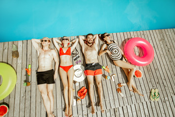 Group of a happy friends in swimwear lying on the poolside, sunbathing near the swimming pool, view from above