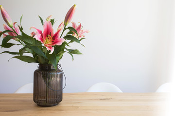 pink lily flowers in a vase on a wooden table in the interior against a white wall in modern room