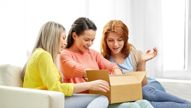 delivery and friendship concept - three teenage girls or friends opening parcel box at home