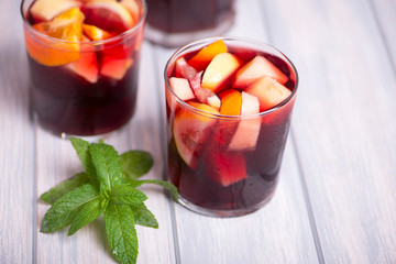 Two glasses next to jug with sangria and a mint leaf on wooden table. Typical Spanish drink made with wine and fruits.