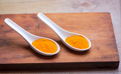 Two white spoons on brown wooden kitchen board. Healthy orange spice.