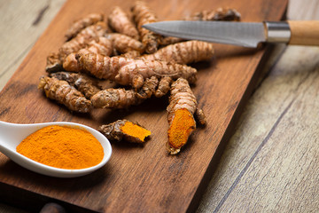 Turmeric roots next to knife and spoon on cutting board in the kitchen. Specia for health and cooking ingredient.