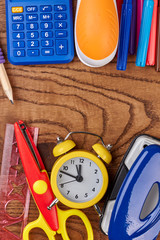 School or office supplies on wooden background. Alarm clock, calculator and different stationery...