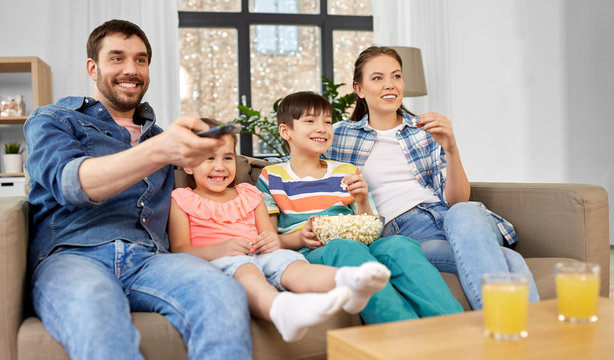 Family, Leisure And People Concept - Happy Mother, Father, Son And Daughter With Popcorn Watching Tv At Home