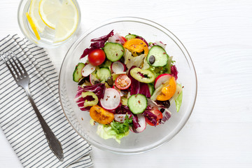 Salad with tomatoes, cucumbers, peppers, herbs and lemonade on white table. Healthy food concept