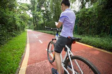 Cyclist using smart phone while riding bike on the summer forest trail
