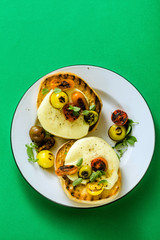 melted cheese sandwich on grilled bread with caramelized multi-colored cherry tomatoes and fresh sage on a green background