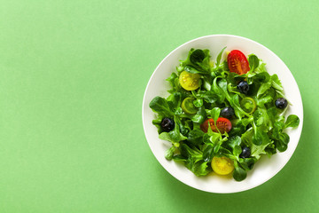 fresh salad of arugula and valerian leaves with colored tomatoes and blueberries in a plate on a green background.