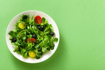 fresh salad of arugula and valerian leaves with colored tomatoes and blueberries in a plate on a green background.