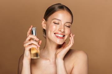 Image of adorable half-naked woman smiling at camera and holding face oil