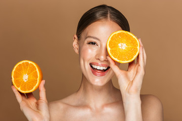 Image closeup of healthy half-naked woman smiling and holding two orange parts