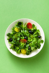 fresh salad of arugula and valerian leaves with colored tomatoes and blueberries in a plate on a...