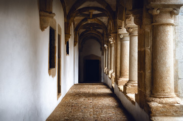 Passagge through an antique medieval cloister with white wall and stone columns, leading to a distant door in an old portuguese monastery