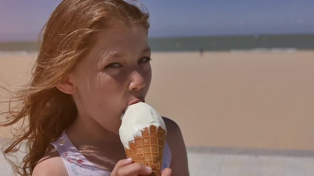 jolie fillette d&eacute;gustant une cr&egrave;me glac&eacute;e sur la plage ensoleill&eacute;e
