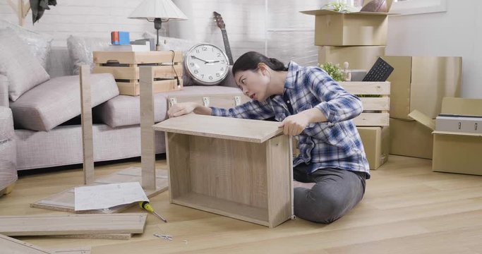 slow motion of frustrated asian woman reading instruction assembly furniture sitting in apartment living room relocation. DIY wood shelf in new home. confused young girl with wooden board putting