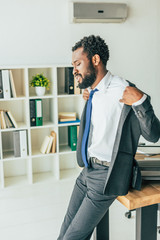 Fototapeta premium exhausted african american businessman undressing while suffering from heat in office