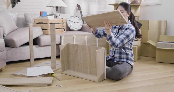 young unhappy woman assembling shelf at home with confused emotion sitting on wooden floor in living room with packing cardboard boxes. frowning lady diy furniture difficult confused puzzled correct