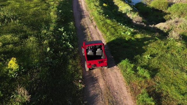 4K Aerial view of a red 4x4 car driving on a dirt mountain road.