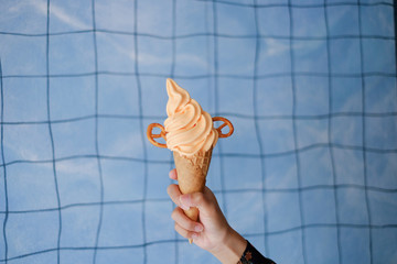 Women hand  holding peach soft serve ice cream cone with waffle cone on blue background. selective focus - Powered by Adobe