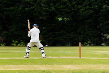 Behind side view of cricket player batting while playing on field in a local park
