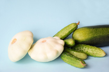 Summer green zucchini, cucumbers and white pattypan squash on a light blue background with space for text. Still-life of summer harvest. Vegetarians and vegetable trade, kitchen concept.