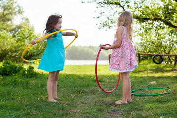 children play with hula Hoop and train their skills in summer. Cheerful Exercise Concept . happy girls having fun with hula hoops outdoor. activity for the baby concept. Funny summer games for kids