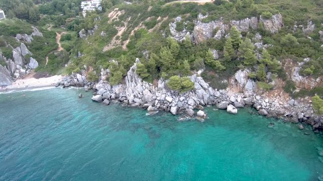 Aerial view of small beach with turquoise water next to rocks and trees in the area of Agia Paraskevi Halkidiki, Greece