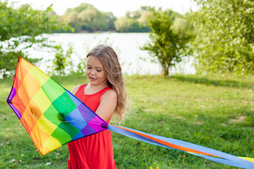 Child playing with a kite while running outdoors, sunset, in summer day. Funny time with family. Happy little girl launch a kite