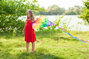 Child playing with a kite while running outdoors, sunset, in summer day. Funny time with family. Happy little girl launch a kite 